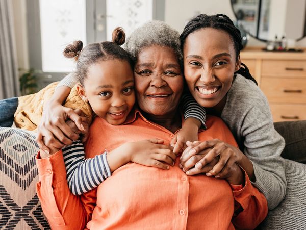 Three generations of women sharing a warm embrace and smiles on a couch.