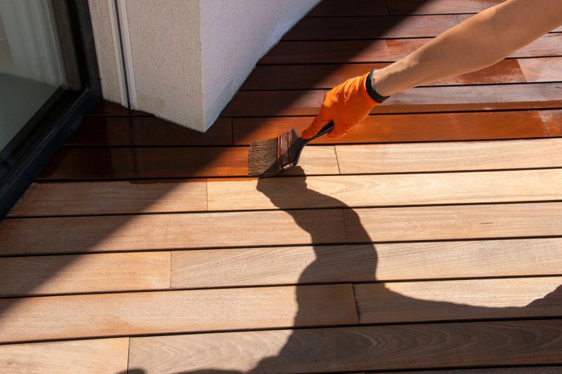 Deck sealing, worker hand applying a wood stain, close up of hand with paintbrush painting wood planks, hardwood floor restoration