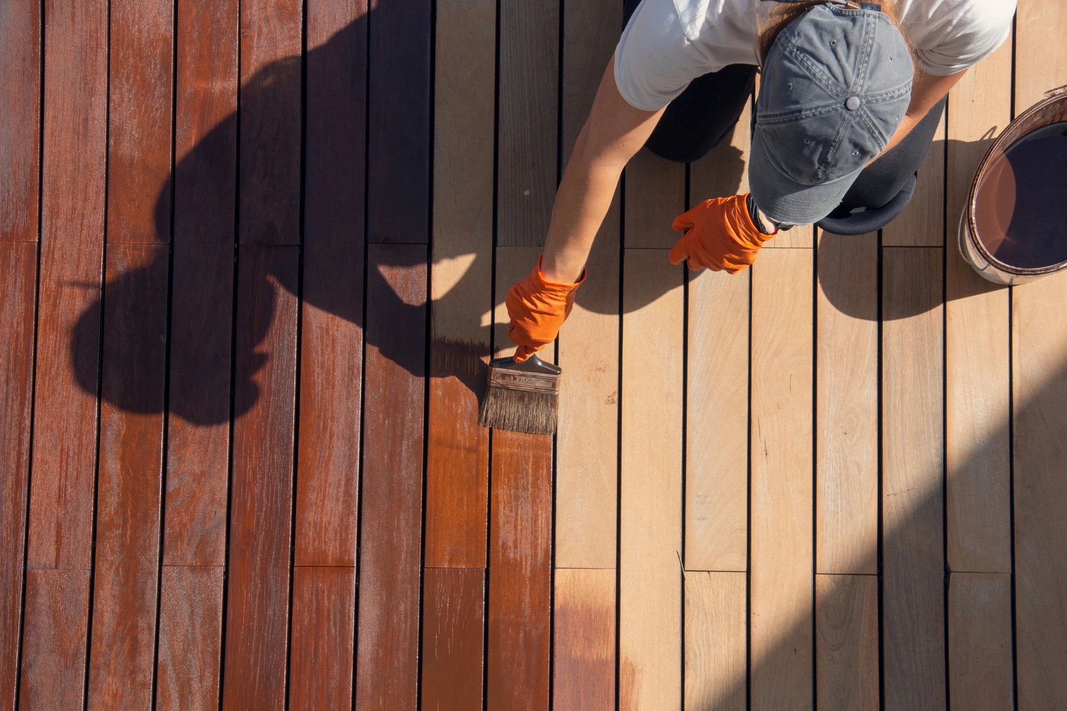 Person staining a wooden deck with protective finish.