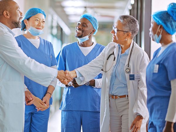 Medical professionals shaking hands in a hospital hallway, showing teamwork and collaboration.