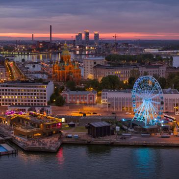 Evening cityscape with a lit Ferris wheel and historic buildings by the waterfront.