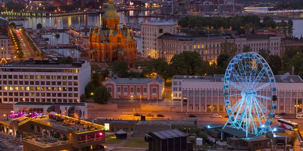 Evening cityscape with illuminated Ferris wheel and historic church by the water.