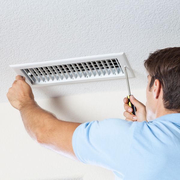 Person removing air vent register vent screws with a screwdriver