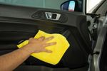 Person cleaning car interior door with yellow cloth.