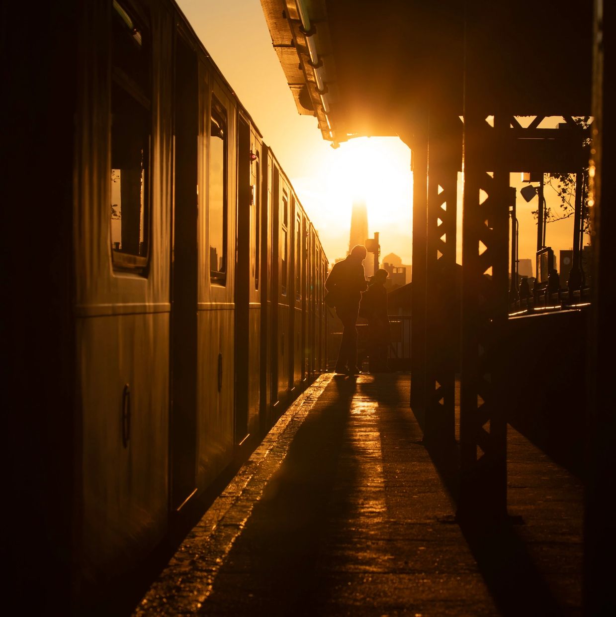 Silhouettes of people waiting by a train during golden hour.