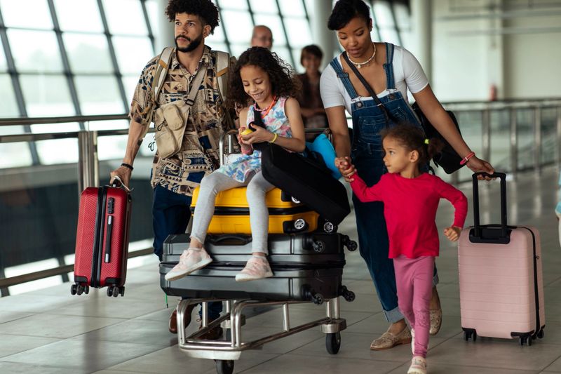 Parents and their kids are walking with luggage to the airport.
