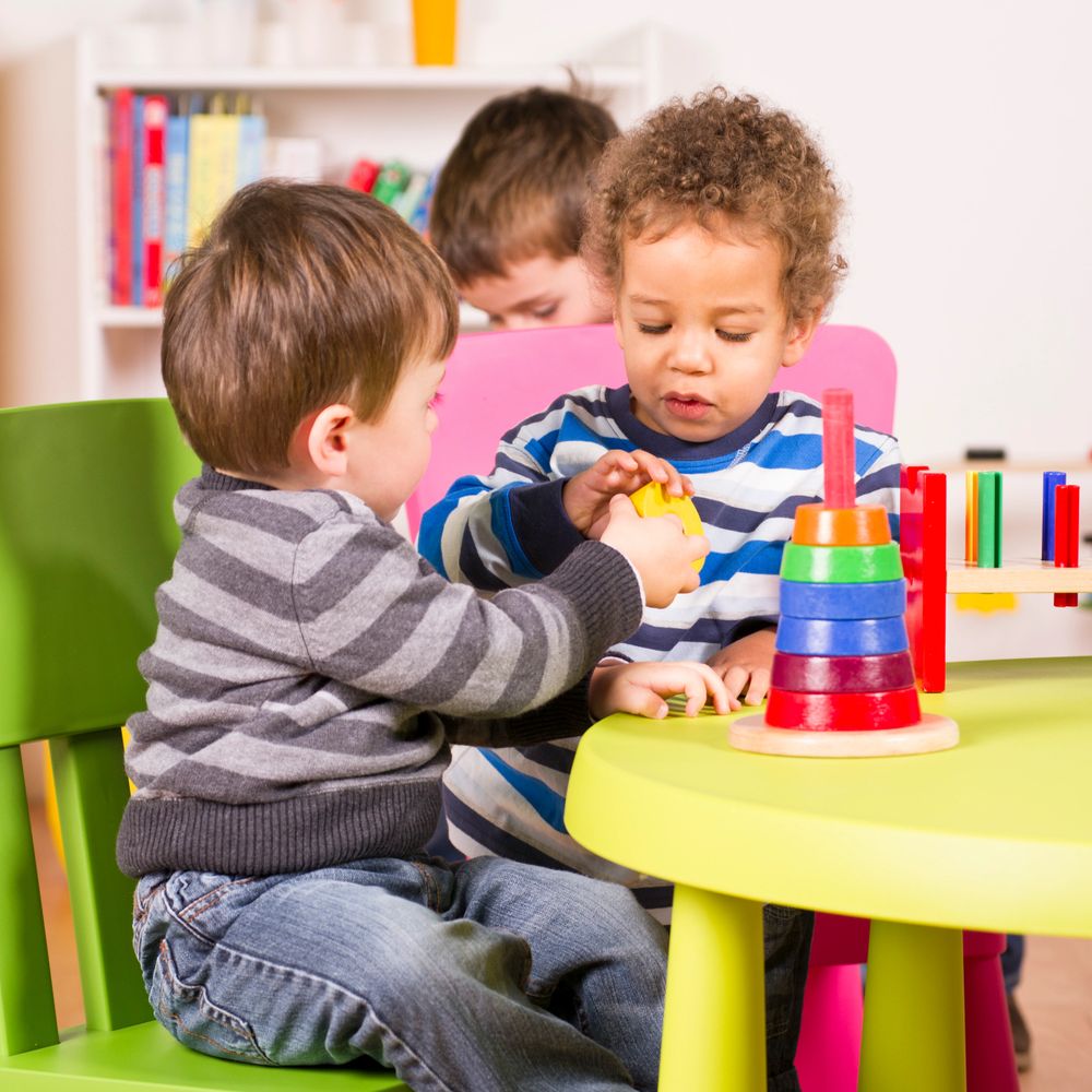 Two young boys playing with a stacking toy at a colorful table.