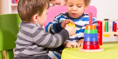 Two young children playing with colorful stacking toys at a table.
