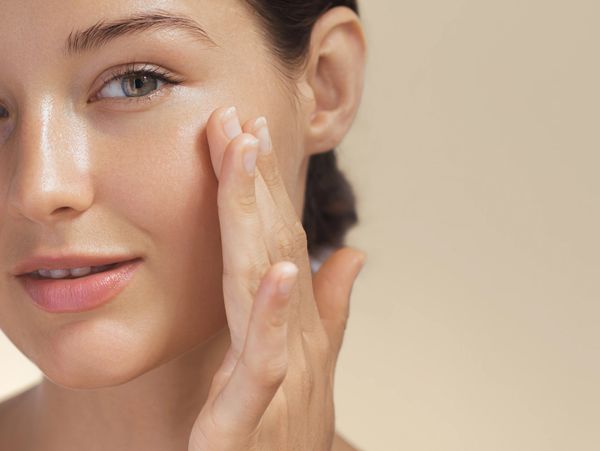Young woman applying skincare cream on her face with a gentle smile.