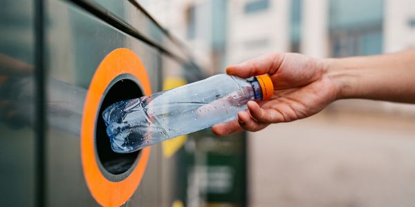Hand placing a plastic bottle into a recycling bin with an orange rim.