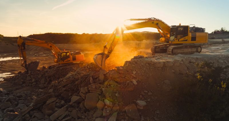 Aerial Drone Shot Of Construction Site On Sunny Day: Industrial Excavators Digging Rocks To Lay Foundation For An Apartment Building. People Using Heavy Machinery To Complete A Real Estate Project.