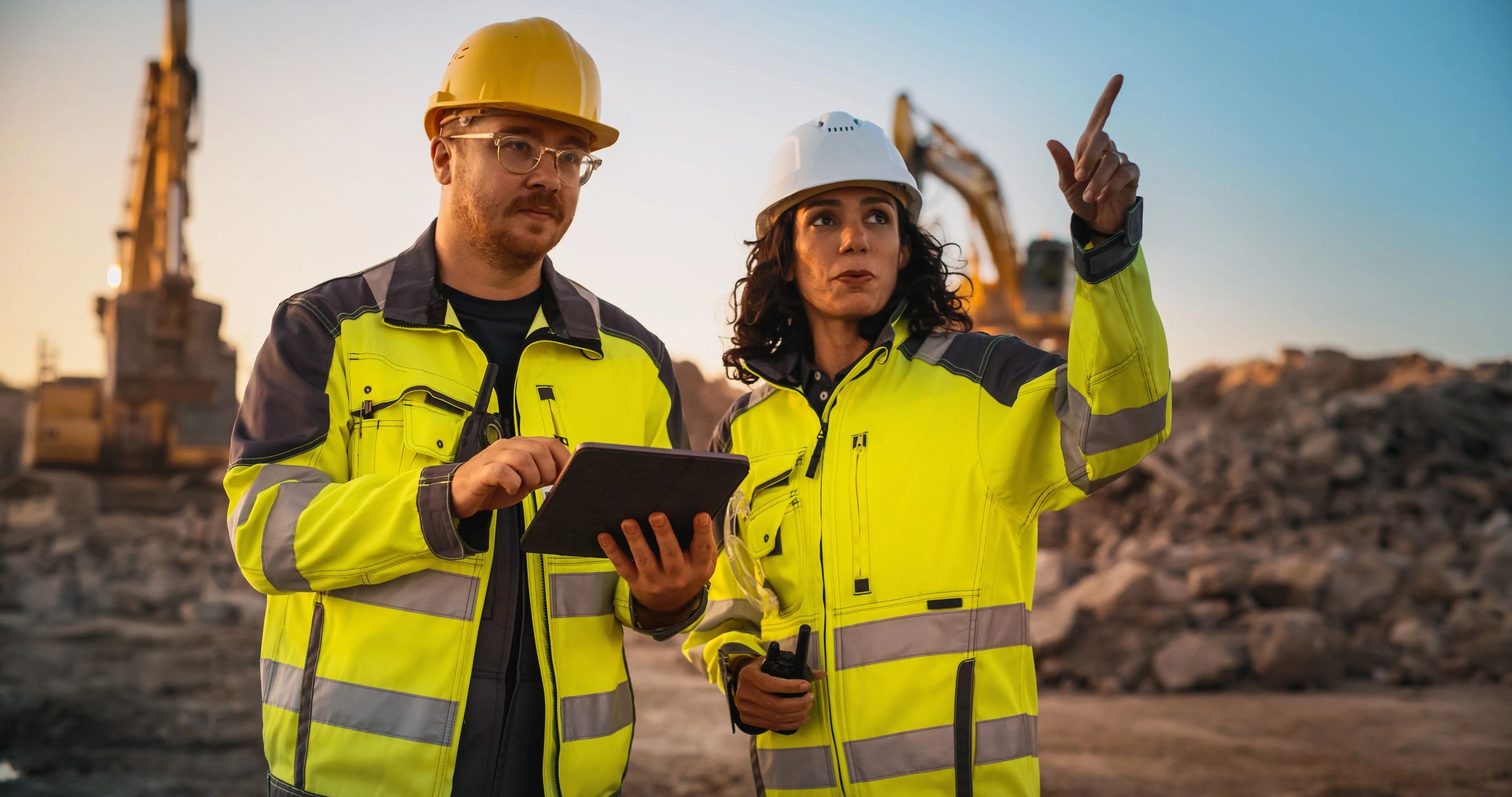 Two construction workers in safety gear reviewing plans onsite.