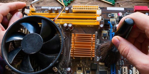 Hands cleaning a computer motherboard with a brush and handling RAM sticks.