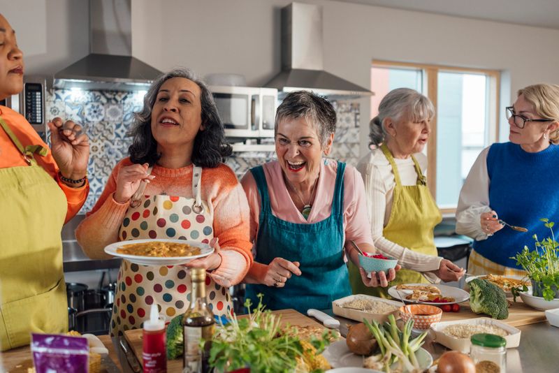 A group of mature and senior women enjoying a staycation and taking part in a cooking class in Amble, North East England. They are all bonding and laughing with each other while they try the dish they have all helped to make.Videos also available for this scenario.