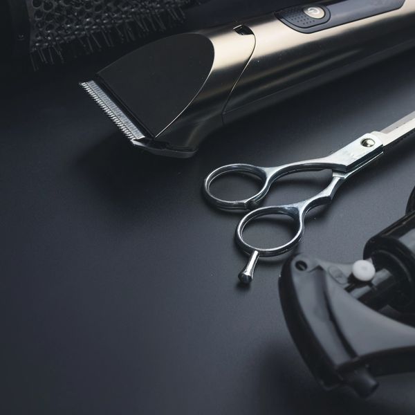 Hairdressing tools including clippers, scissors, and spray bottle on a dark surface.