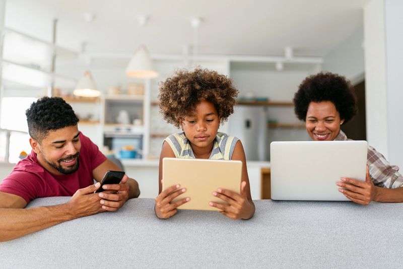 Obsessed to tech devices happy african american family using digital tablet, computer, smartphones.
