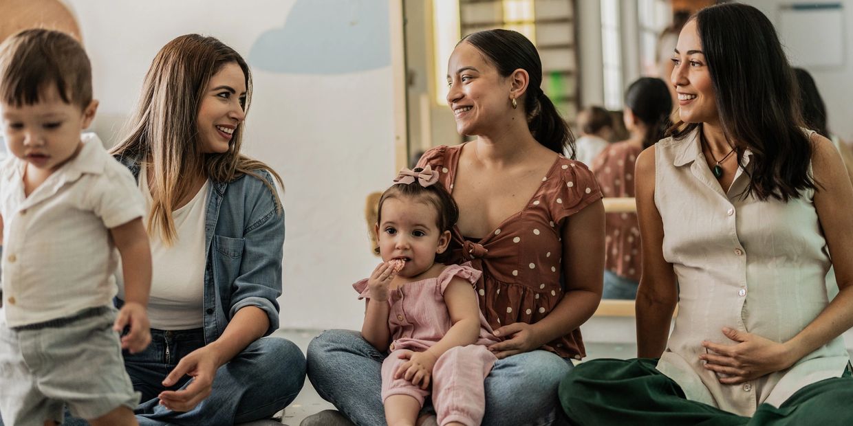 Three women and two children sitting and interacting indoors.