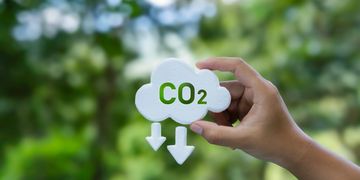 Hand holding a cloud-shaped sign with CO2 and downward arrows.
