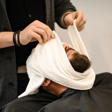 Barber wrapping a towel around a man's face during grooming.
