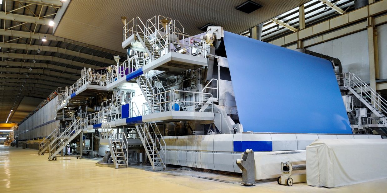 Large industrial paper machine producing wide blue paper rolls.