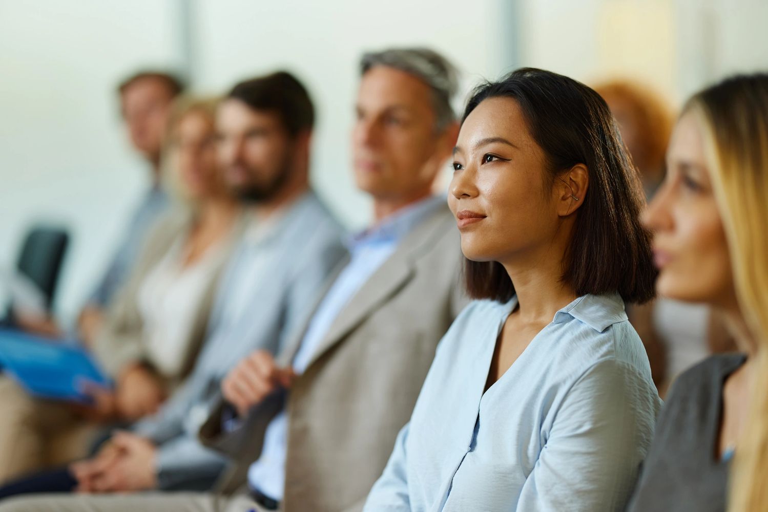 A focused young woman listens attentively in a diverse group meeting.