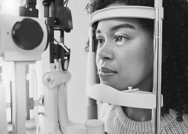 young girl with dark curly hair having her eyes examined on a slit lamp