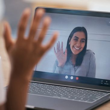 Person waving during a video call on a laptop.