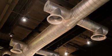 Metallic air ducts and vents on a ceiling in an industrial setting.