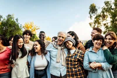 A diverse group of people laughing and embracing outdoors on a sunny day.