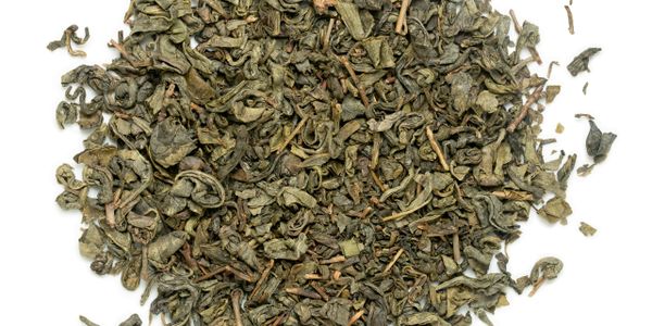 A pile of loose dried green tea leaves with stems on a white background.