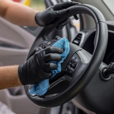 Person wearing gloves cleaning a car steering wheel with a cloth.