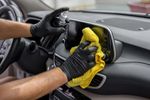 Person cleaning a car dashboard with a yellow cloth.