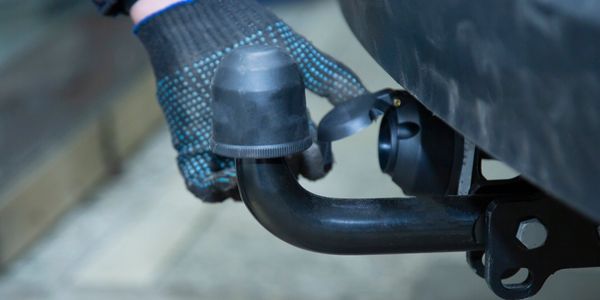 A gloved hand touching a trailer hitch on a vehicle's rear.
