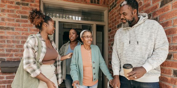 Family warmly greets elderly woman at home entrance.