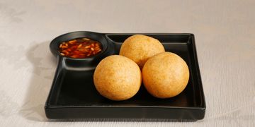 Three golden fried balls served with a dipping sauce on a black tray.