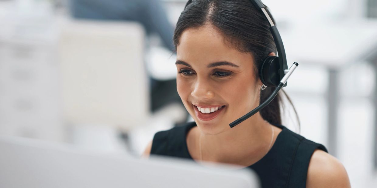 Mujer sonriente con auriculares y micrófono trabajando en computadora.