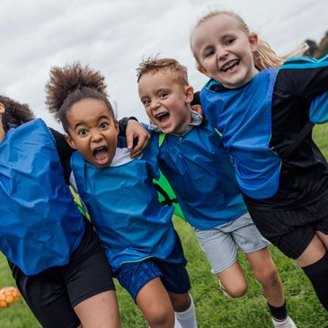 Joyful kids in blue sports vests celebrating on a soccer field.