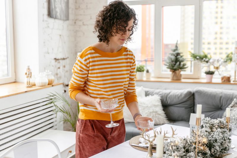 Woman setting up dining table decorated for Christmas with fir branches and candles
