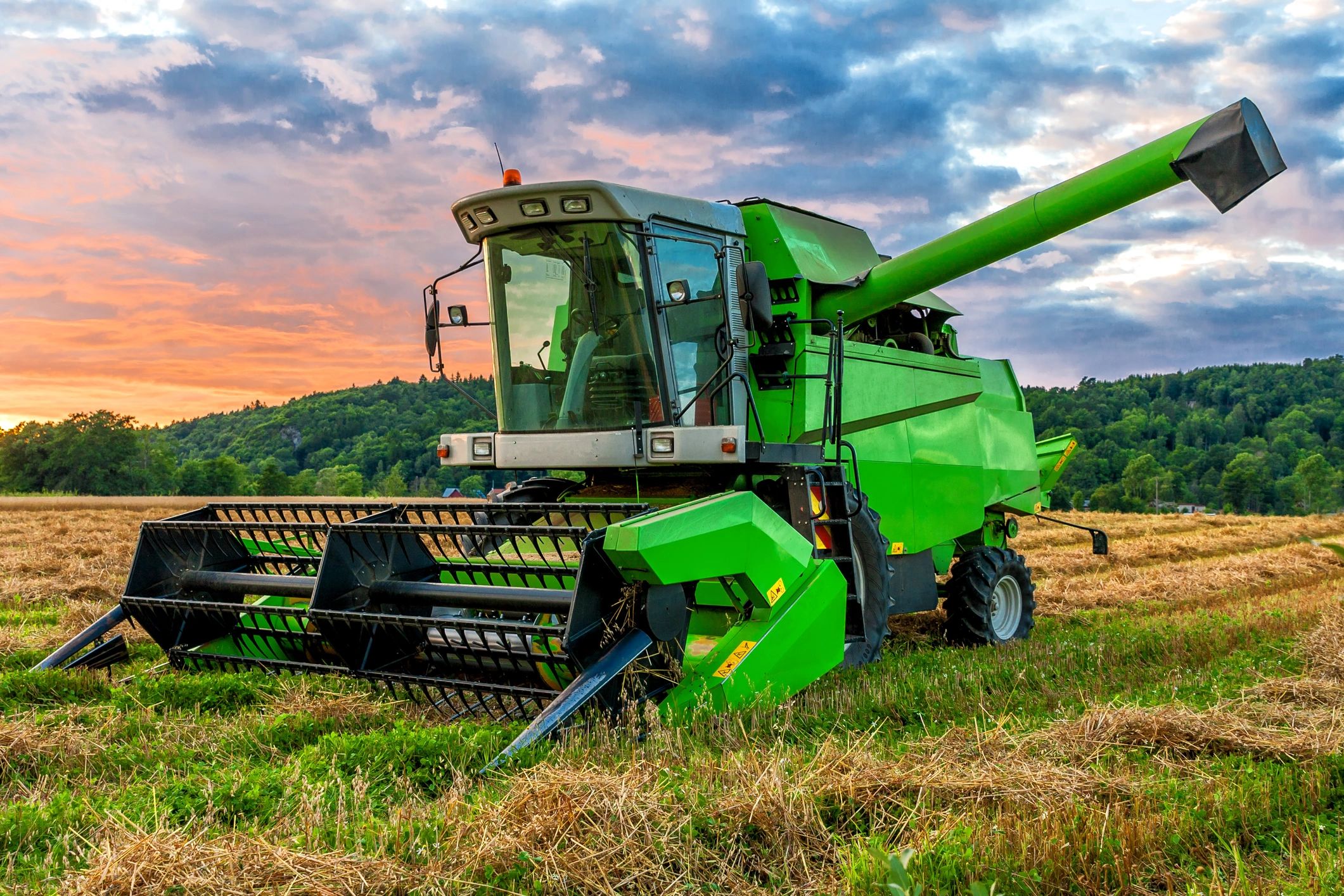 Green combine harvester in a field at sunset.