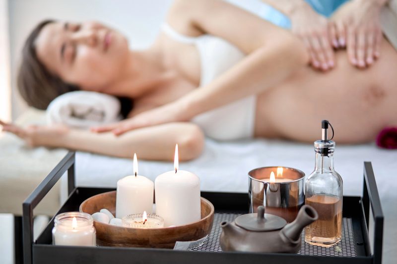 Pregnant woman at the physiotherapist cabinet getting massage, in spa salon. Light Bright room with candles, focus on candles