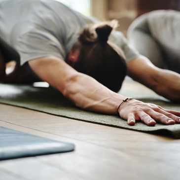Person stretching forward on a yoga mat indoors.