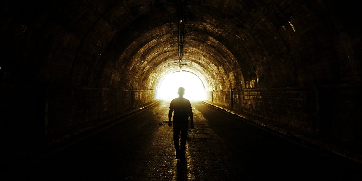Silhouette of a person walking towards a bright tunnel exit.