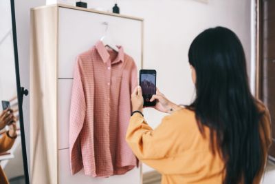 Person taking a photo of a pink shirt on a hanger.