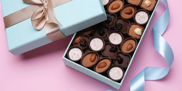 Elegant blue box of assorted chocolates with nuts and cream fillings, on a pink background.