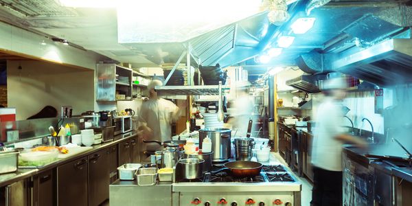 Busy commercial kitchen with chefs at work and stainless steel appliances.