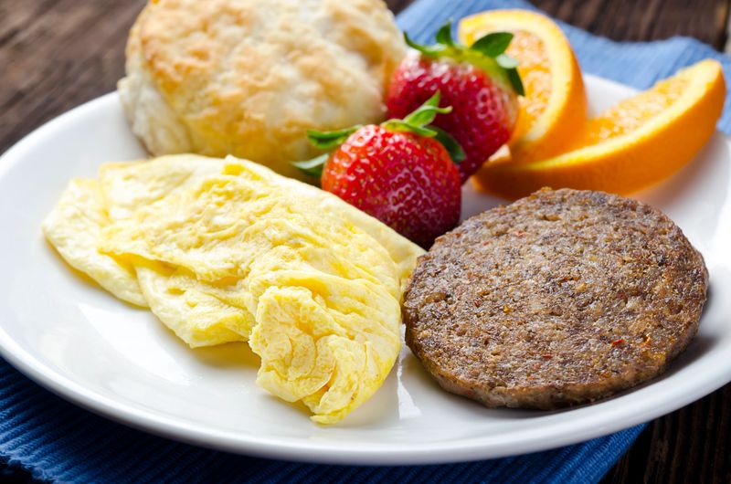 "Traditional Breakfast of Scrambled Eggs, Sausage Patties, Buttermilk Biscuit, Strawberries and Orange Slices."