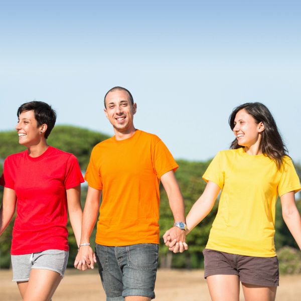 Three friends holding hands outdoors, wearing colorful shirts and smiling.