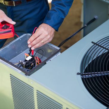 Technician using a multimeter to check an air conditioning unit's electrical components.