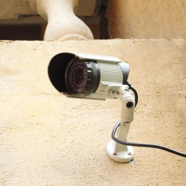 Close-up of a security camera mounted on a textured beige wall.