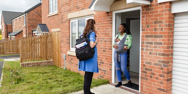 Home visits to a new mother holding her baby in a sling at the doorstep. Home support.